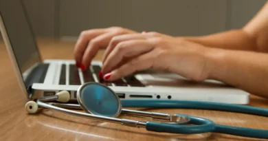 Médica digita no computador, tendo seu estetoscópio ao lado. Foto: National Cancer Institute/Unsplash