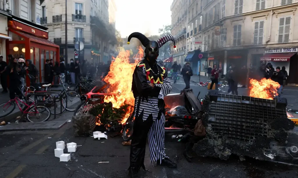 A demonstrator wearing a costume stands in front of burning flames, in Paris, France, October 18, 2026. REUTERS/Abdul Saboor