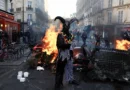 A demonstrator wearing a costume stands in front of burning flames, in Paris, France, October 18, 2026. REUTERS/Abdul Saboor