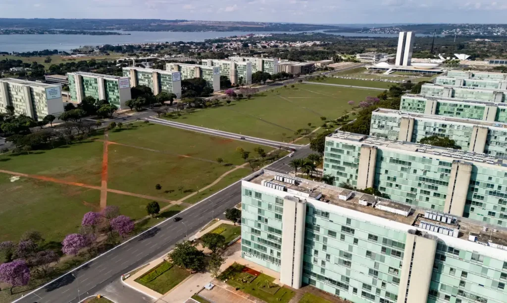 22/06/2026 - Brasília - A floração dos ipês-roxos transforma a paisagem de Brasília em um espetáculo de cores que dura apenas algumas semanas, mas deixa marcas na memória durante todo o ano. Considerada uma das árvores mais simbólicas do Cerrado brasileiro, o ipê anuncia a chegada da estação seca justamente quando perde suas folhas e exibe flores em tons vibrantes que contrastam com o céu azul da Esplanada dos Ministérios. Em meio às linhas retas, ao concreto aparente e aos tons cinza característicos da arquitetura modernista idealizada por Oscar Niemeyer, os ipês surgem como protagonistas da paisagem urbana. A explosão de flores roxas quebra a monotonia das formas e colore avenidas, parques e áreas residenciais, criando uma das cenas mais marcantes da capital federal. Breve e intensa, a floração dos ipês lembra que alguns dos mais belos espetáculos da natureza são também os mais passageiros. Foto: Rafa Neddermeyer/Agência Brasil