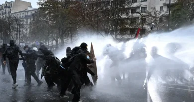 Protesters take cover behind a plywood board as French riot police use a water canon amid clashes during an authorised demonstration organised by labour unions in Paris as part of nationwide protests called by the