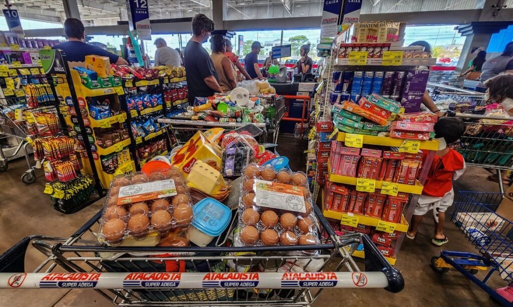 12/06/2026 - Brasília - Consumidores enfrentam longas filas nos caixas de um grande mercado atacadista para finalizar suas compras. Diante do cenário de inflação acumulada e da constante alta de preços nos itens básicos de alimentação, a busca por qualquer tipo de desconto ou promoção tornou-se estratégia essencial para aliviar o orçamento das famílias.Foto: Rafa Neddermeyer/Agência Brasil